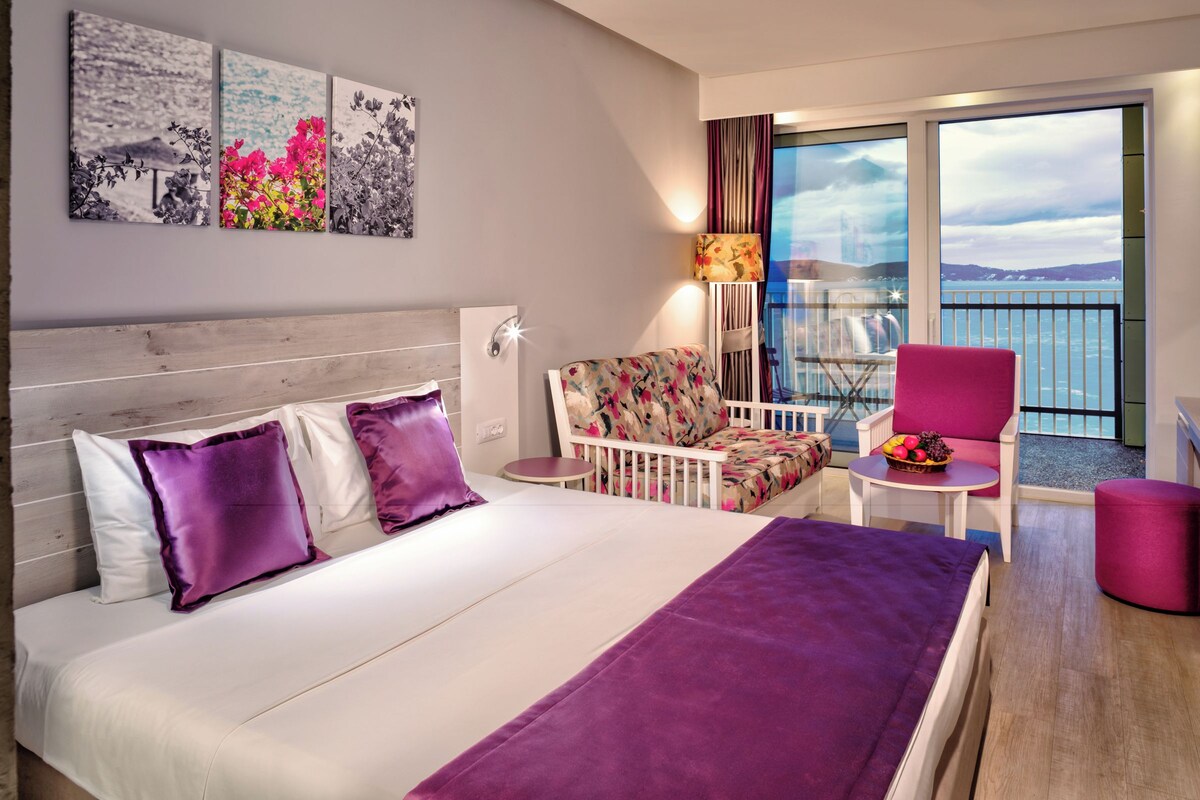 Een hotelkamer met een bed, een stoel, een tafel en een balkon met uitzicht.