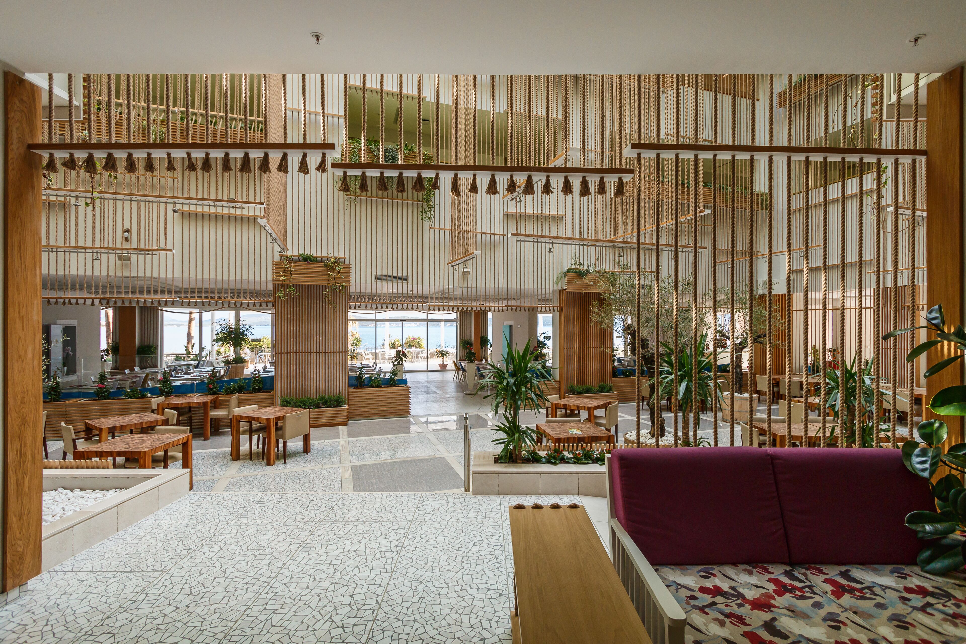 Eine geräumige Lobby mit mehreren Sitzbereichen, einer zentralen Treppe und Blick ins Freie.