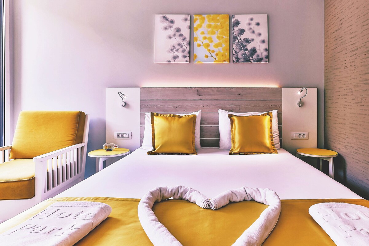 Een moderne hotelkamer met een groot bed, twee nachtkastjes, een stoel en een kunstwerk aan de muur.
