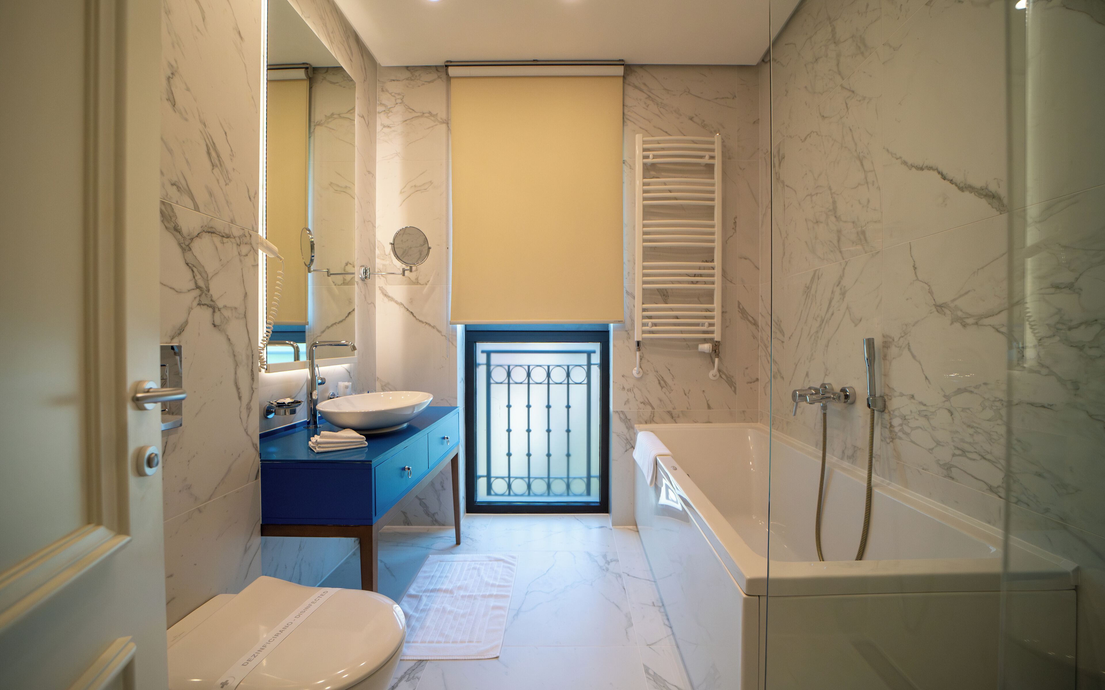 Un baño con piso de mármol, un lavamanos con encimera azul, un inodoro y una bañera con ducha.