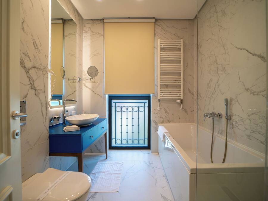 Un baño con piso de mármol, un lavamanos con encimera azul, un inodoro y una bañera con ducha.