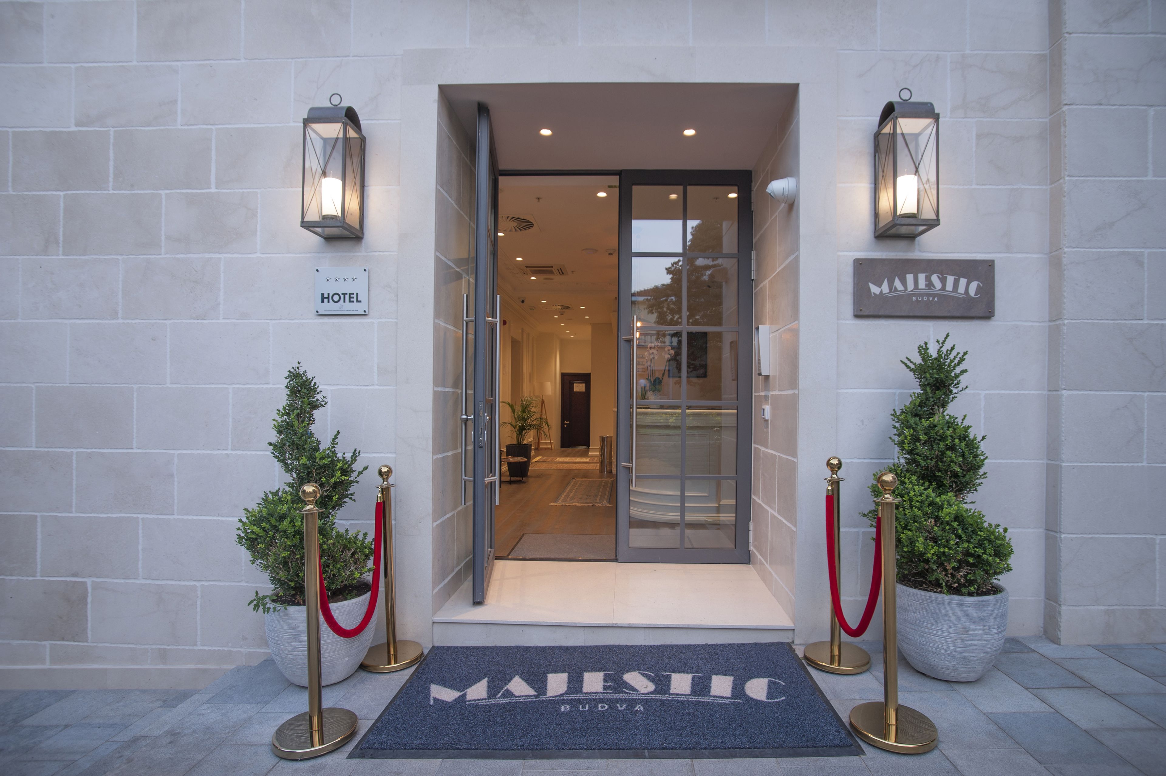 A hotel entrance with a glass door, a red carpet, and a sign that reads "MAJESTIC BUDVA".