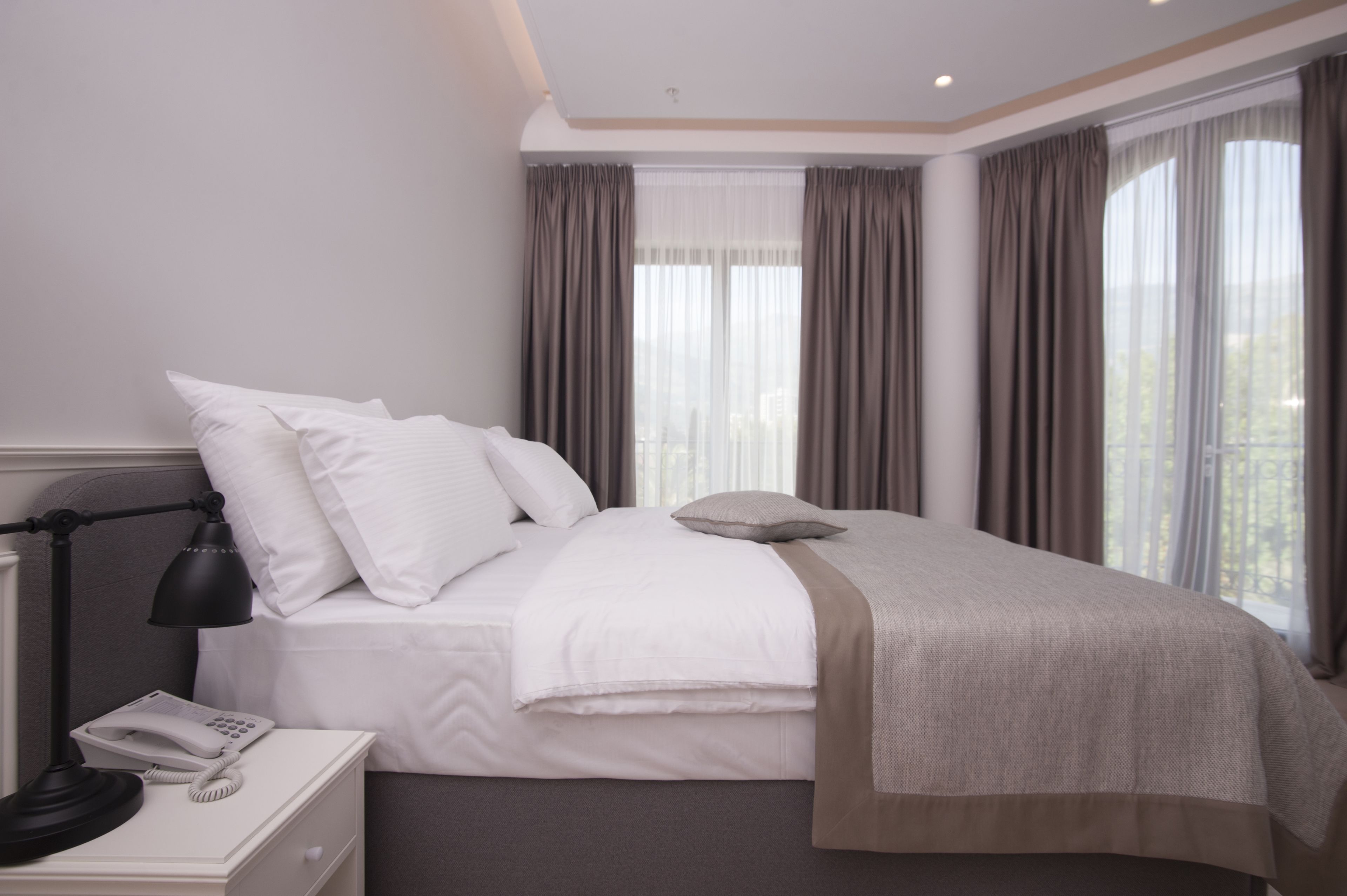 A hotel room with a bed, a bedside telephone, and a window with curtains.