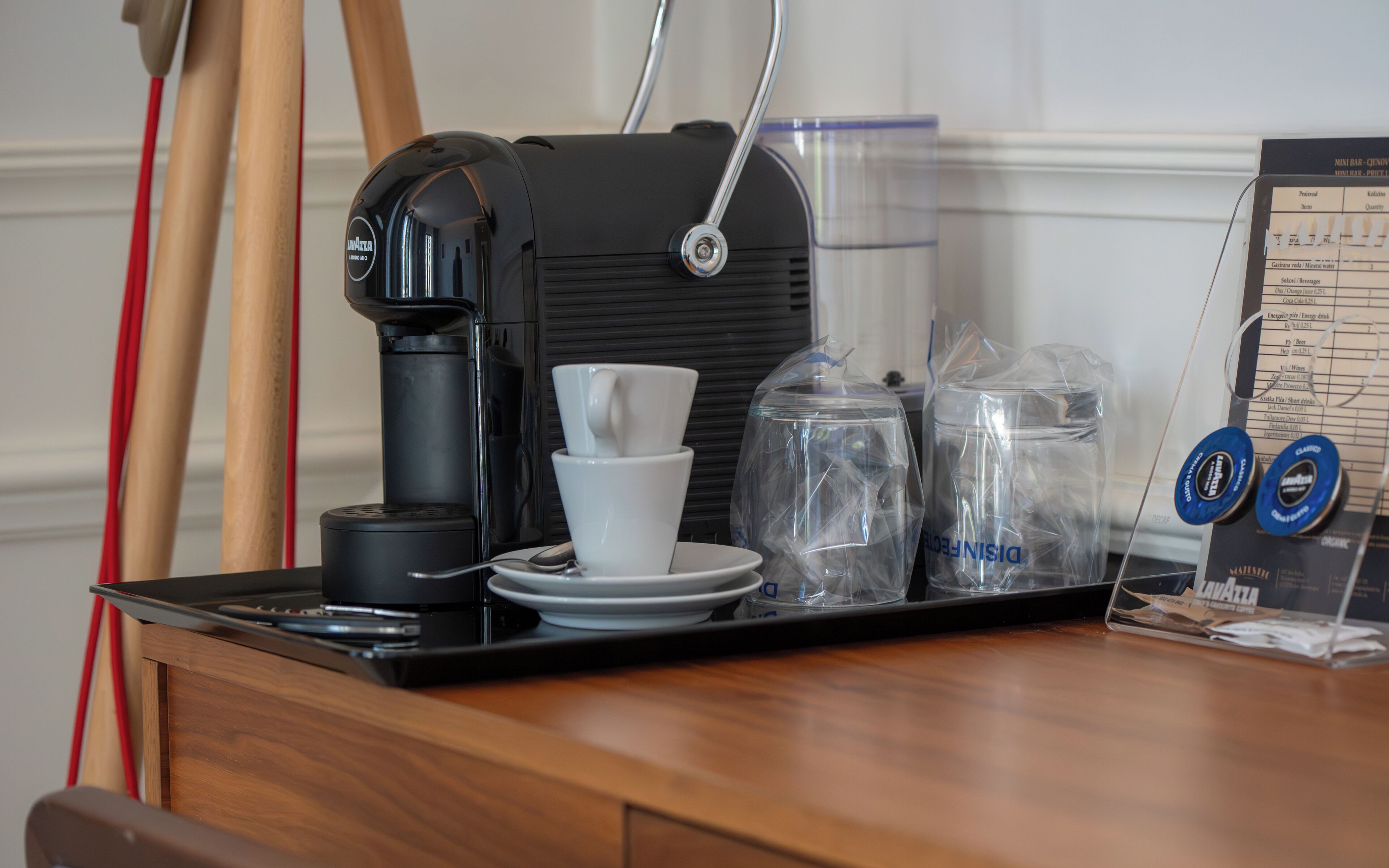 A coffee machine with a cup and saucer, a water dispenser, and a menu on a wooden table.