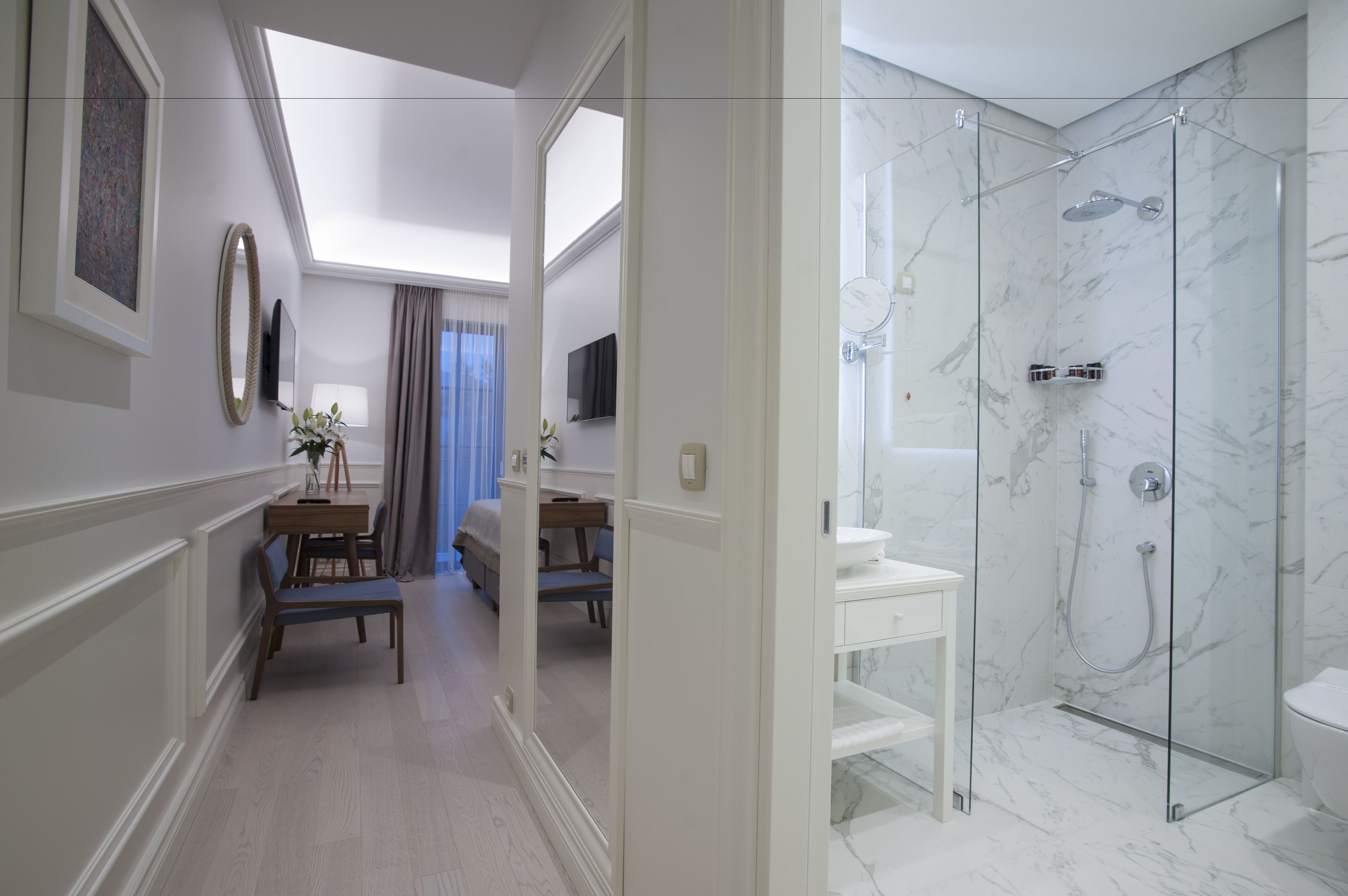 A modern hotel bathroom with a glass-enclosed shower, marble walls, and a white vanity.