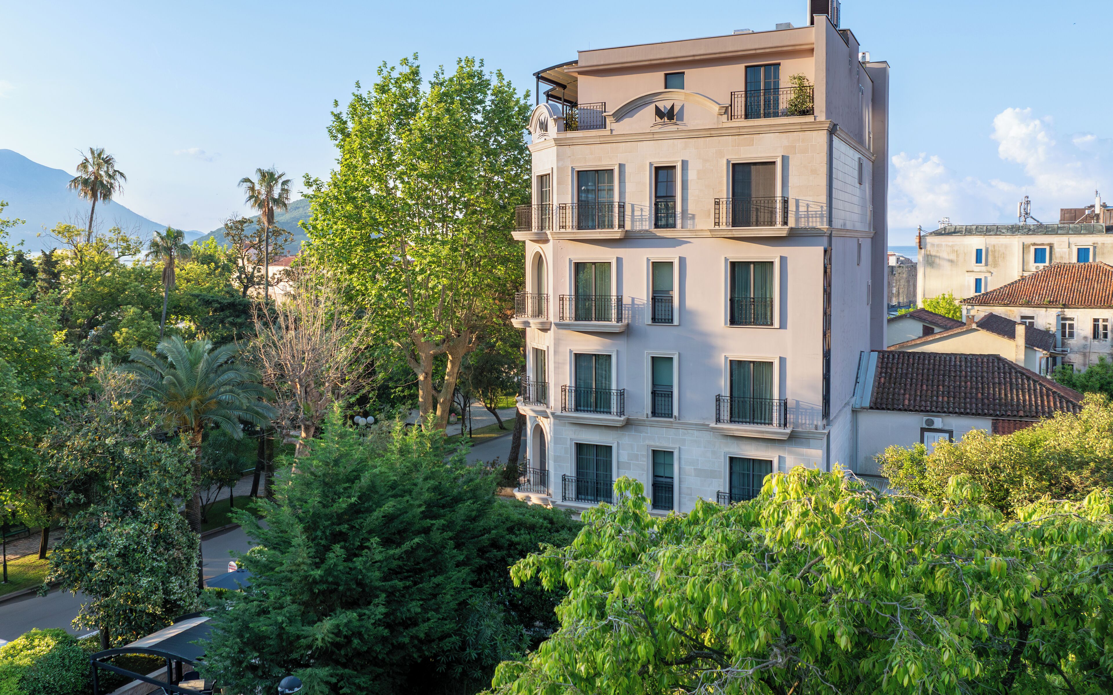 A multi-story building with balconies, surrounded by lush greenery and trees.