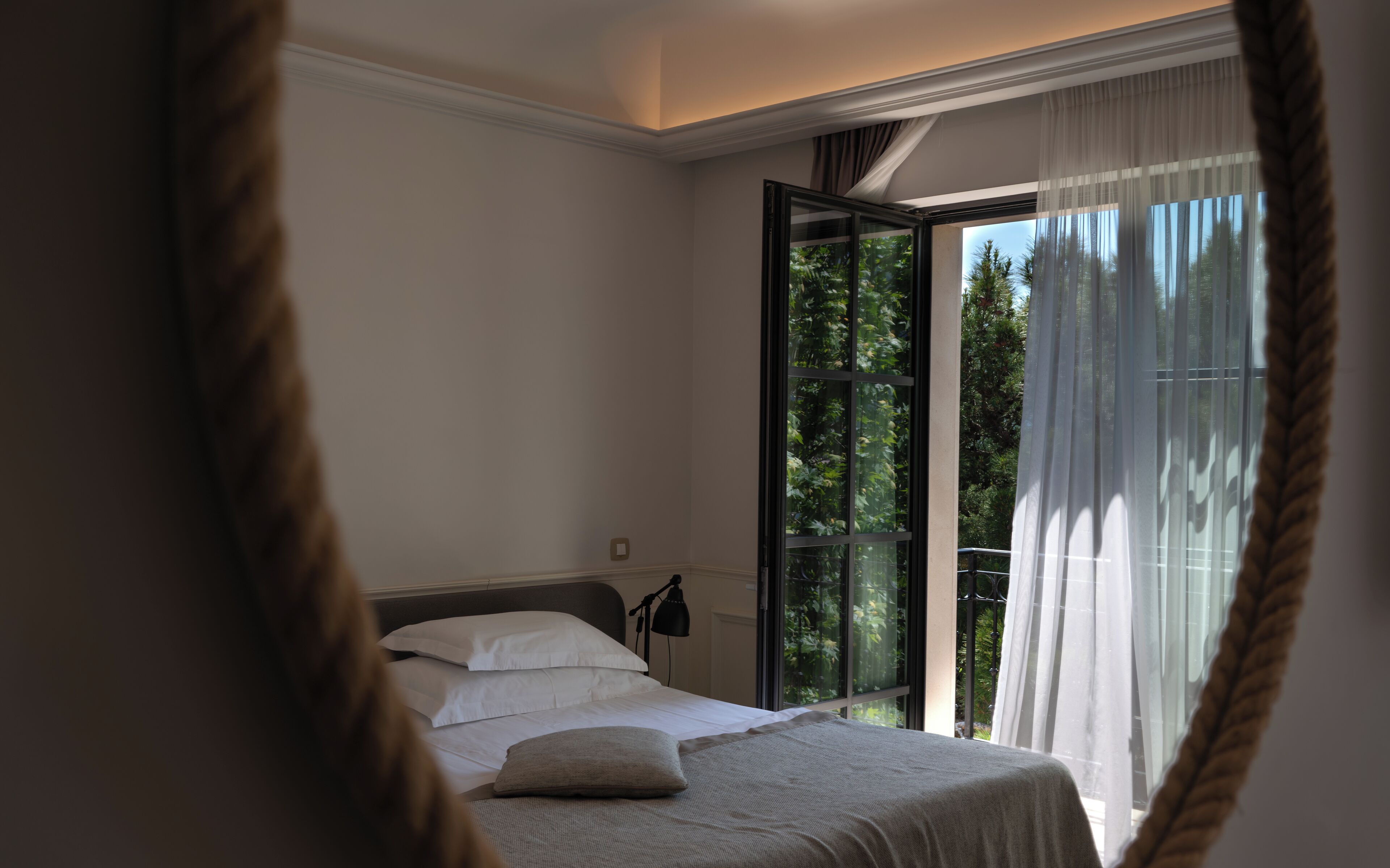 A bedroom with a bed, a nightstand, and a window with a view of greenery.