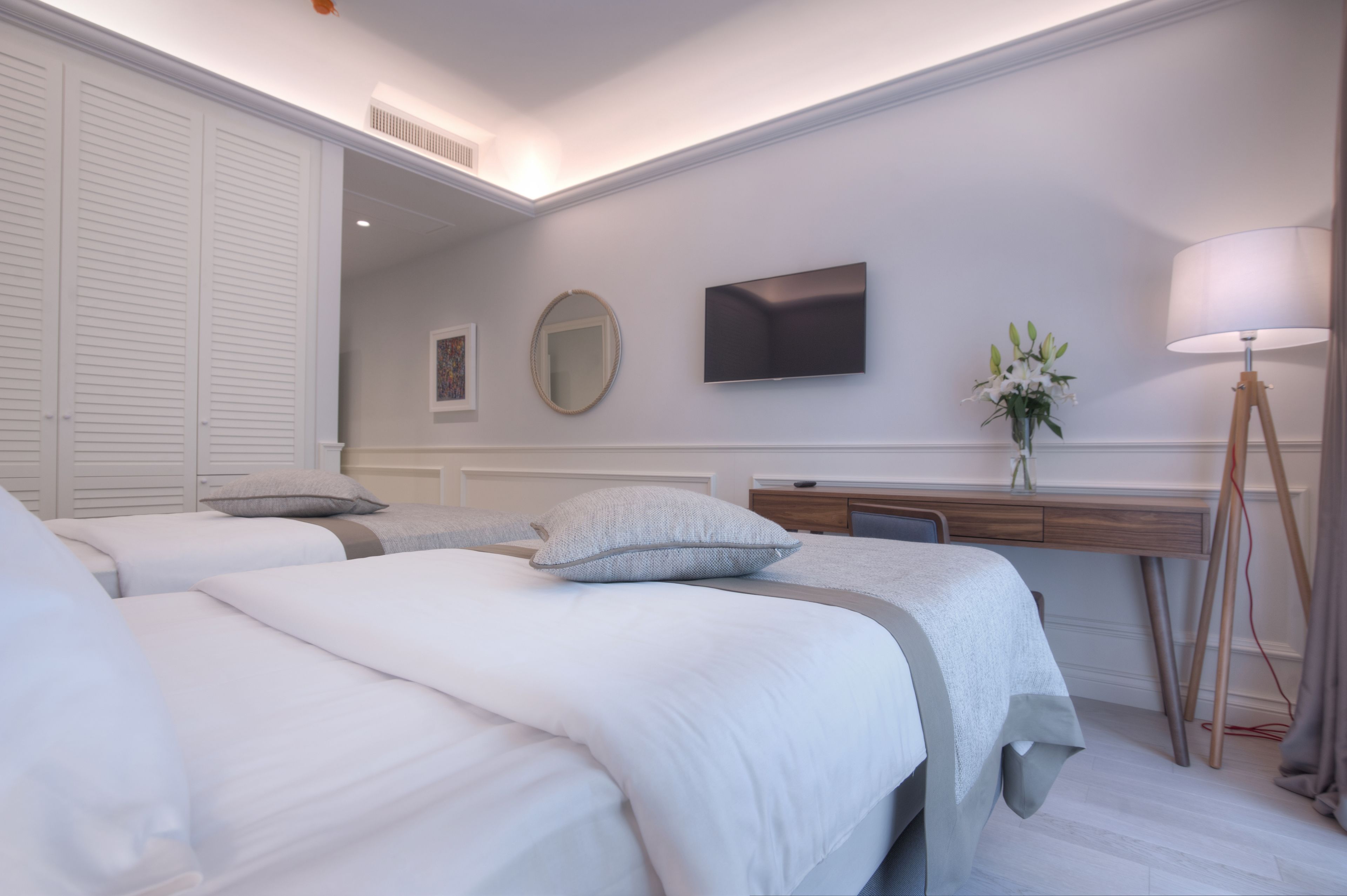 Een moderne hotelkamer met twee bedden, een bureau, een flatscreen-tv, een spiegel en een lamp.