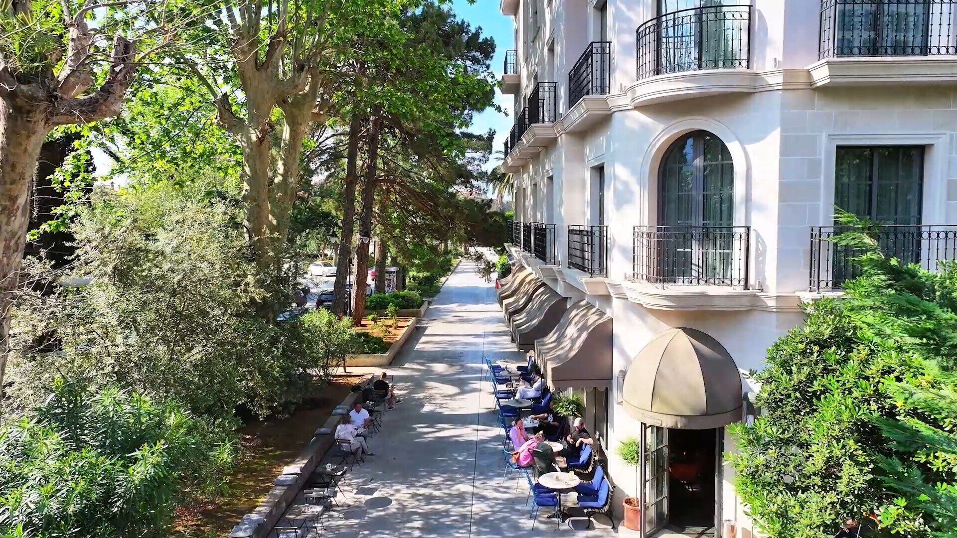 A tree-lined street with outdoor seating and a building with balconies.