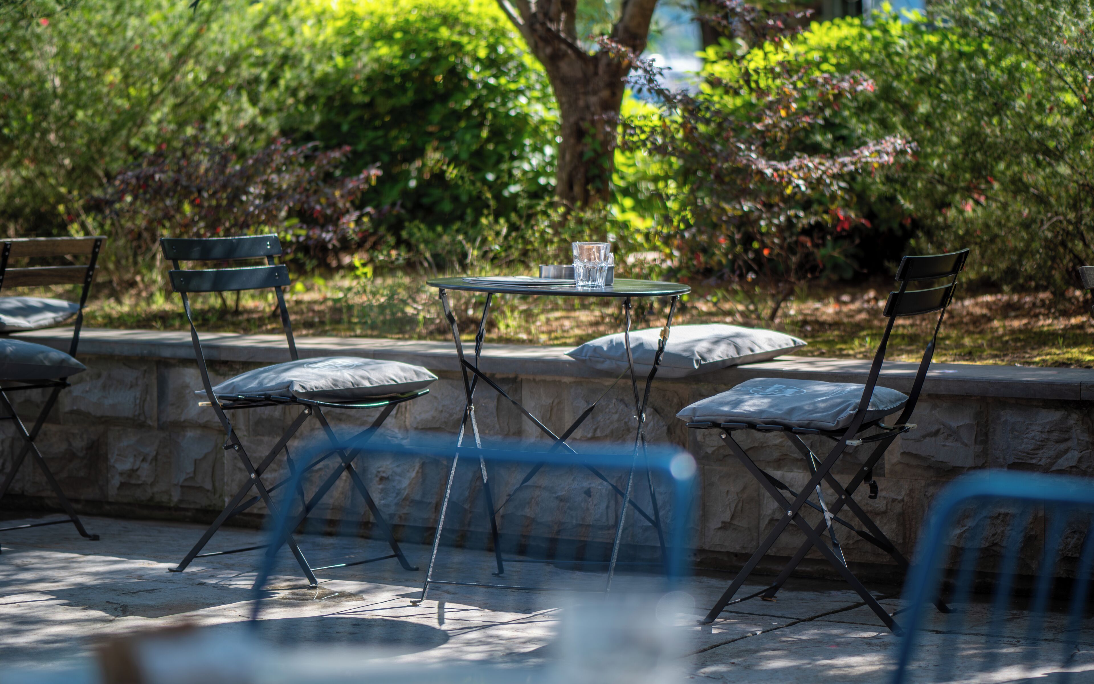 A patio with a table and chairs, surrounded by a stone wall and greenery.