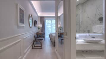 Una habitación de hotel con un pasillo largo que lleva a un baño con un lavamanos de mármol grande y un espejo.