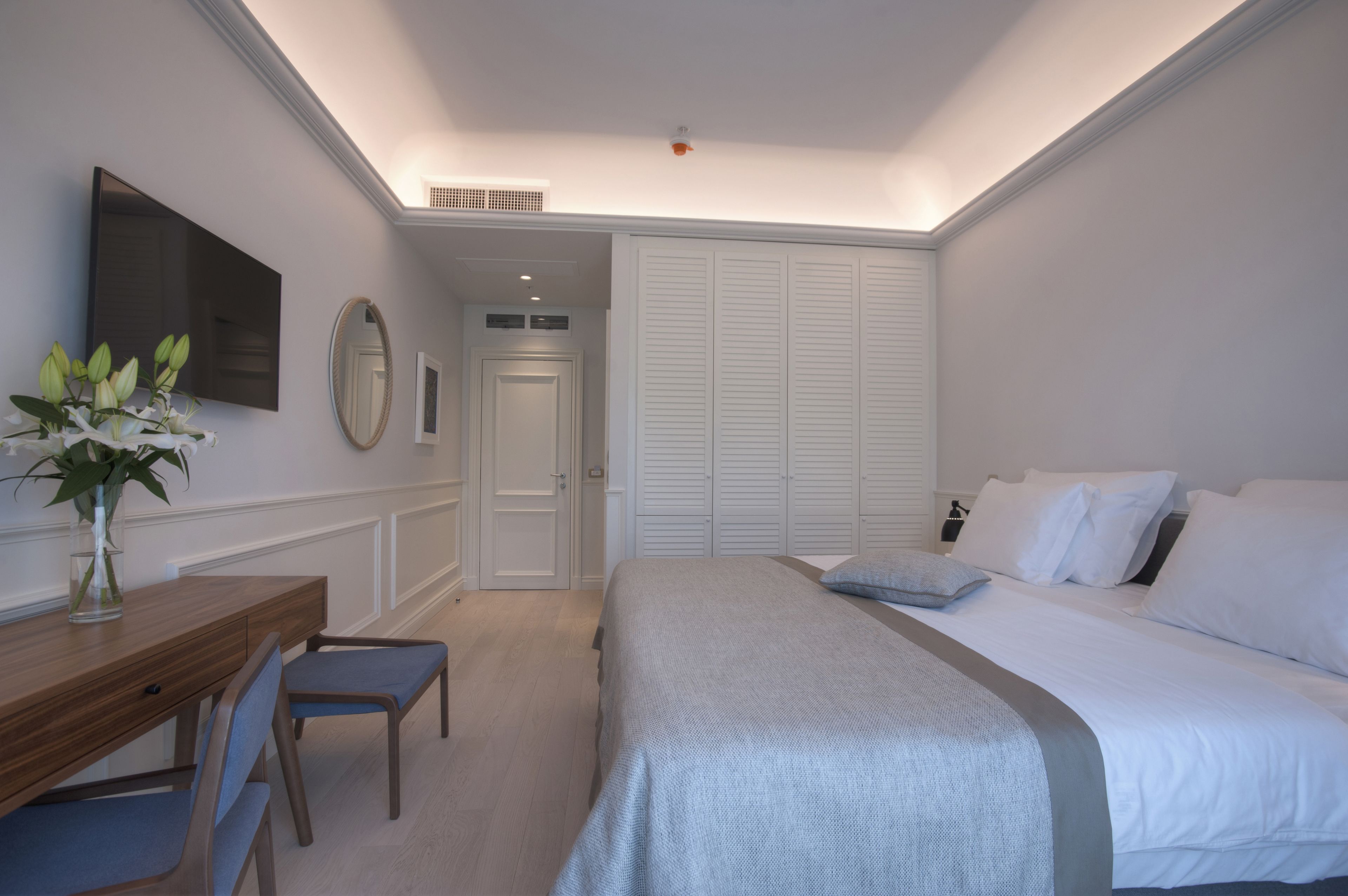 Un dormitorio con cama, mesita de noche, silla y escritorio con un florero.