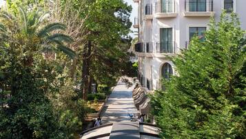 Una calle arbolada con mesas al aire libre y un edificio de varios pisos con balcones.