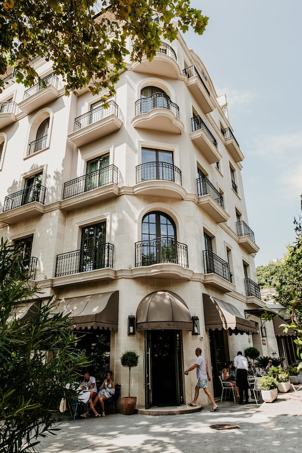 Un hotel de varios pisos con balcones, mobiliario exterior y una entrada principal.