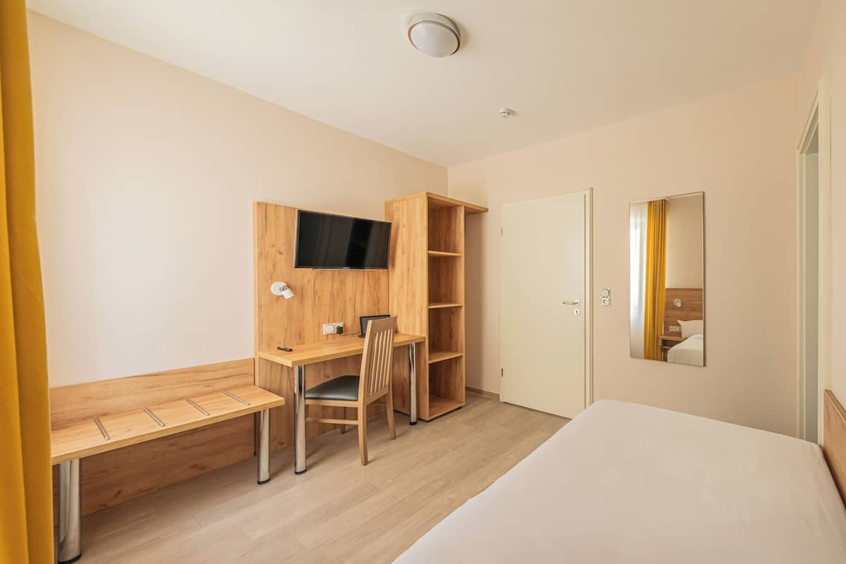 A hotel room with a bed, a desk with a chair, a TV, and a wardrobe.