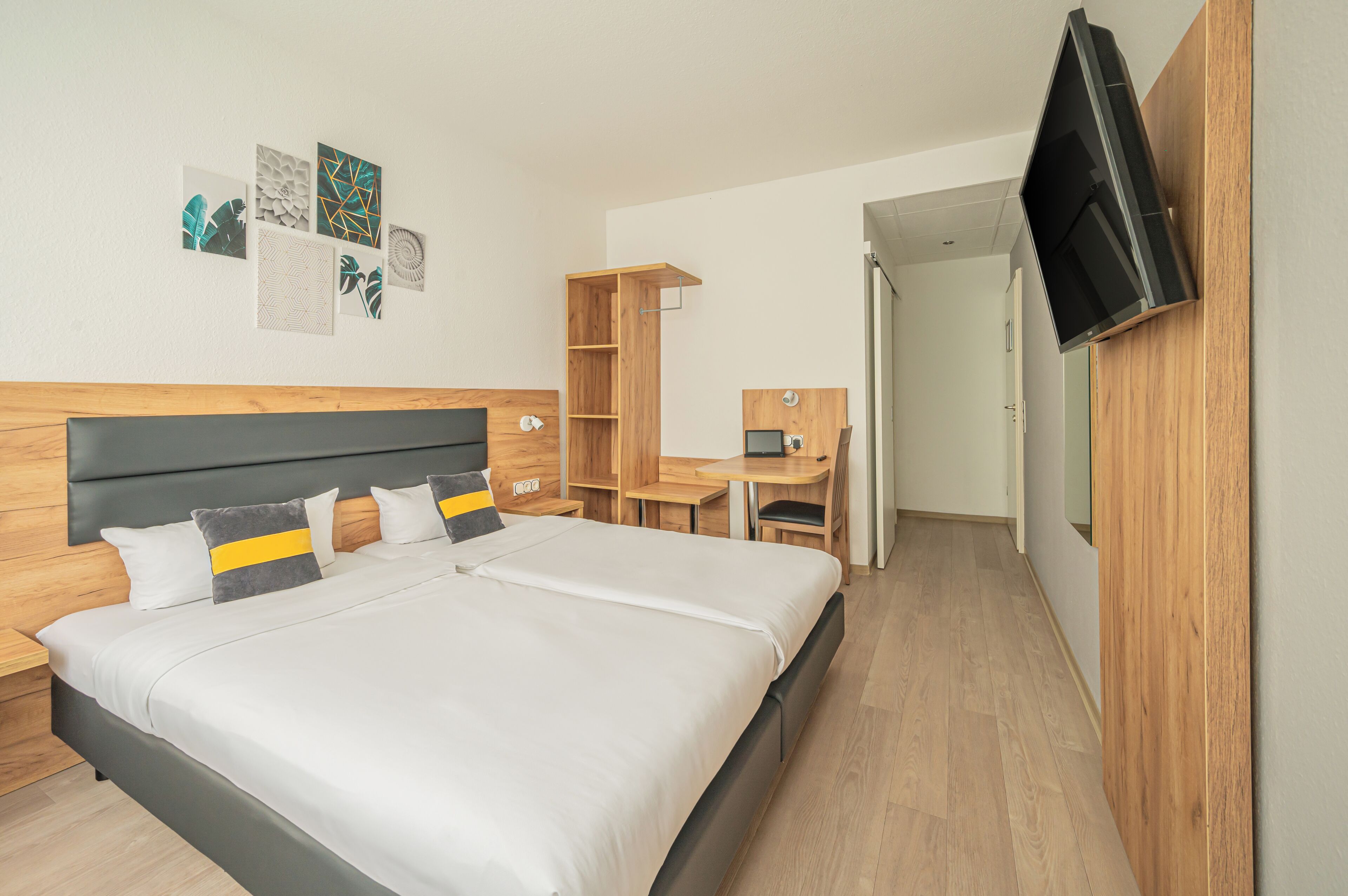 A modern hotel room with a large bed, a desk, and a TV mounted on the wall.