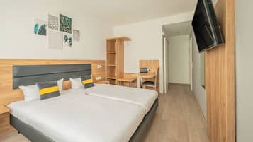 A modern hotel room with a large bed, a desk, and a TV mounted on the wall.