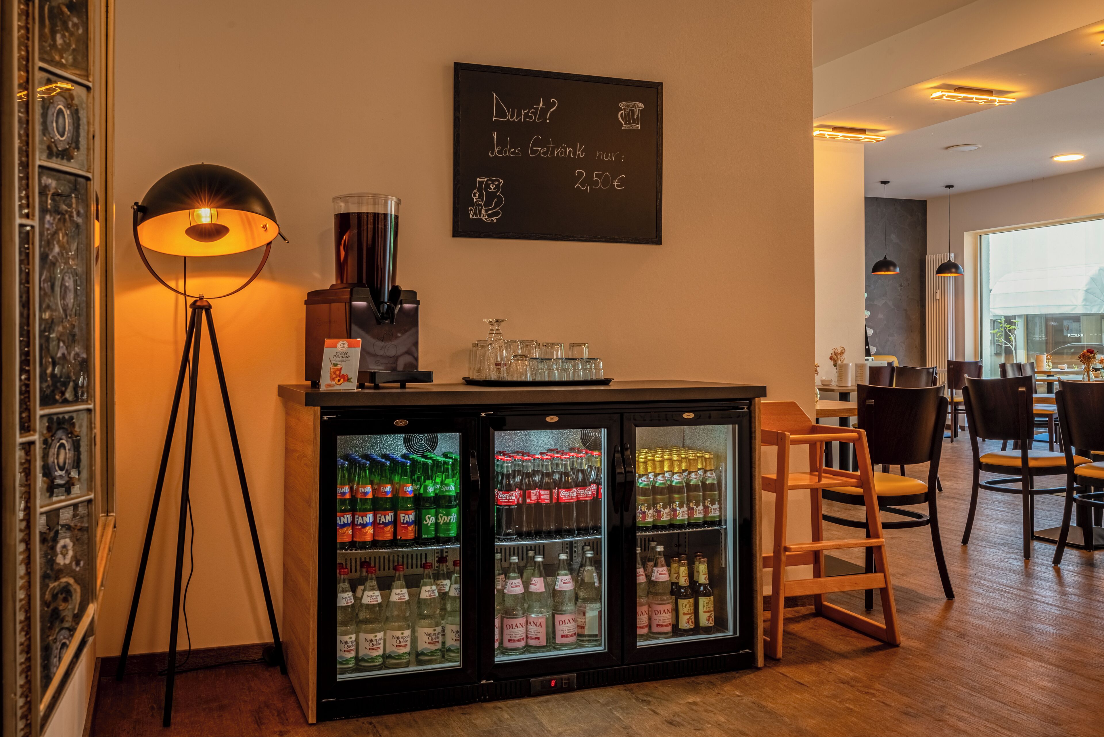 Un espace bar doté d’un tableau noir servant de menu, d’une machine à café et d’un réfrigérateur rempli de boissons.