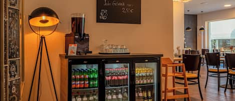 Un espace bar doté d’un tableau noir servant de menu, d’une machine à café et d’un réfrigérateur rempli de boissons.