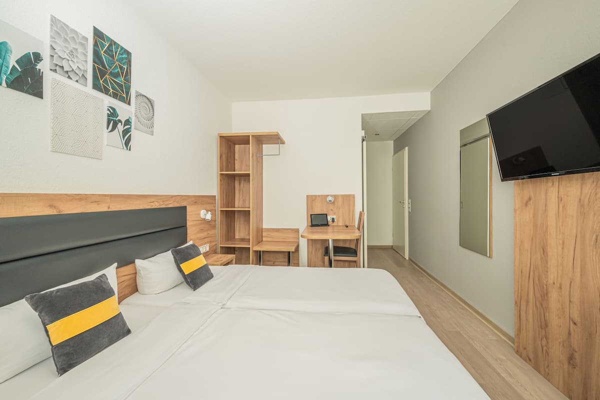 A hotel room with a bed, a desk, a TV, and a wardrobe.