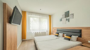 Uma cama de casal com cabeceira de madeira, uma mesa de cabeceira e uma TV fixada na parede.