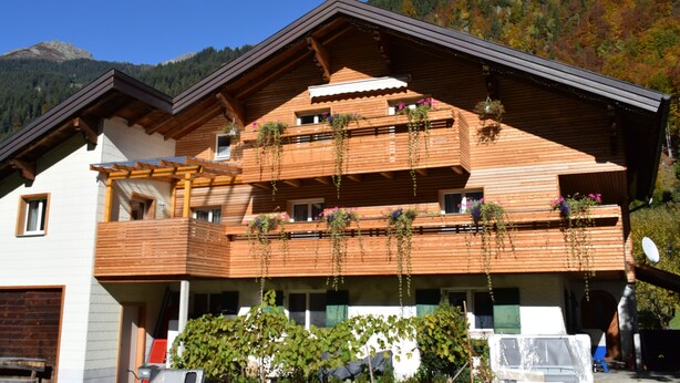 Una cabaña de madera de varios pisos con balcones, rodeada de montañas y follaje otoñal.
