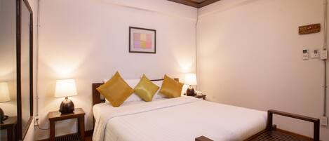 A hotel room with a bed, bedside lamps, a small table, and a wooden bench.