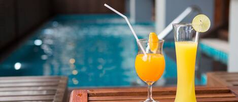 Two drinks on a wooden table near a pool.