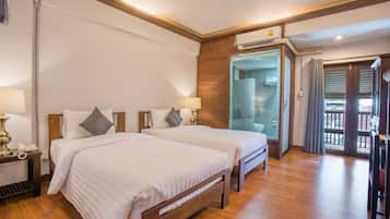 Habitación de hotel con dos camas, suelo de madera, baño con puerta de vidrio y un balcón.