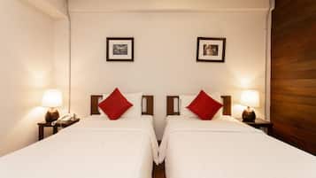 A hotel room with two beds, each with a red pillow and a bedside lamp. There are framed pictures on the wall above the beds.