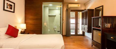 A hotel room with two beds, a wooden floor, a wardrobe, and a bathroom with a glass door.