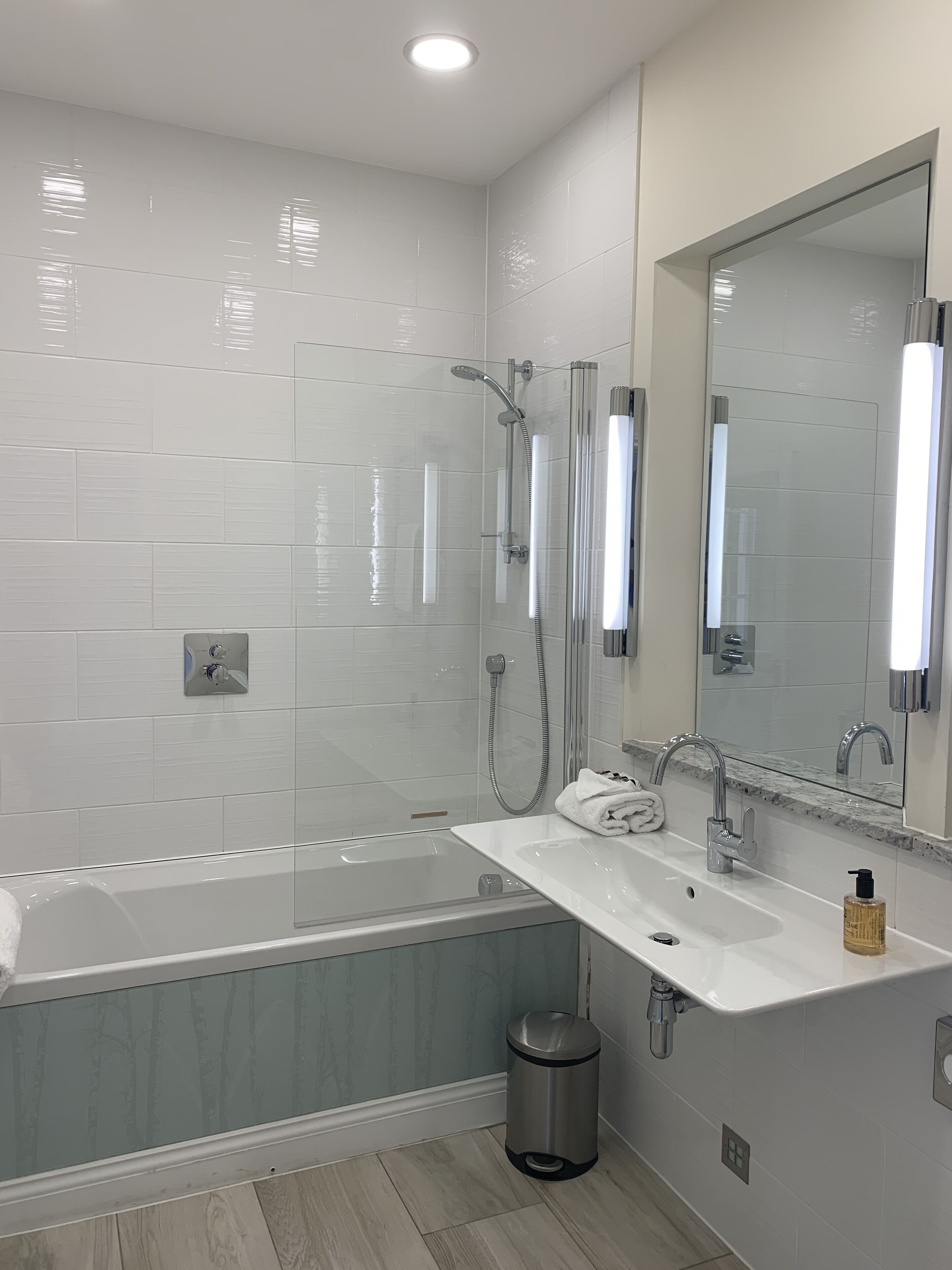 A modern bathroom with a glass-enclosed shower, a white bathtub, a sink with a marble countertop, and a large mirror.