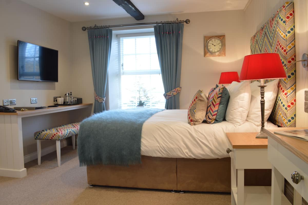 Une chambre à coucher avec un lit, des tables de chevet, un bureau, une télévision et une fenêtre avec des rideaux.