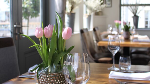 Et spisebord med en vase fyldt med lyserøde tulipaner, et vinglas og et klart glas.