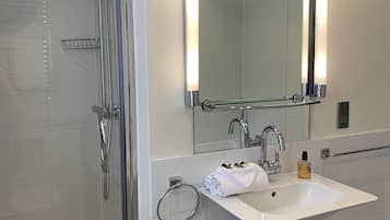Un baño moderno con cabina de ducha de vidrio, un lavabo blanco con espejo y un pequeño cubo de basura.