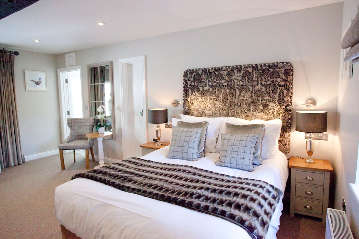 Une chambre bien éclairée avec un grand lit, deux tables de chevet avec des lampes, une chaise et un miroir.