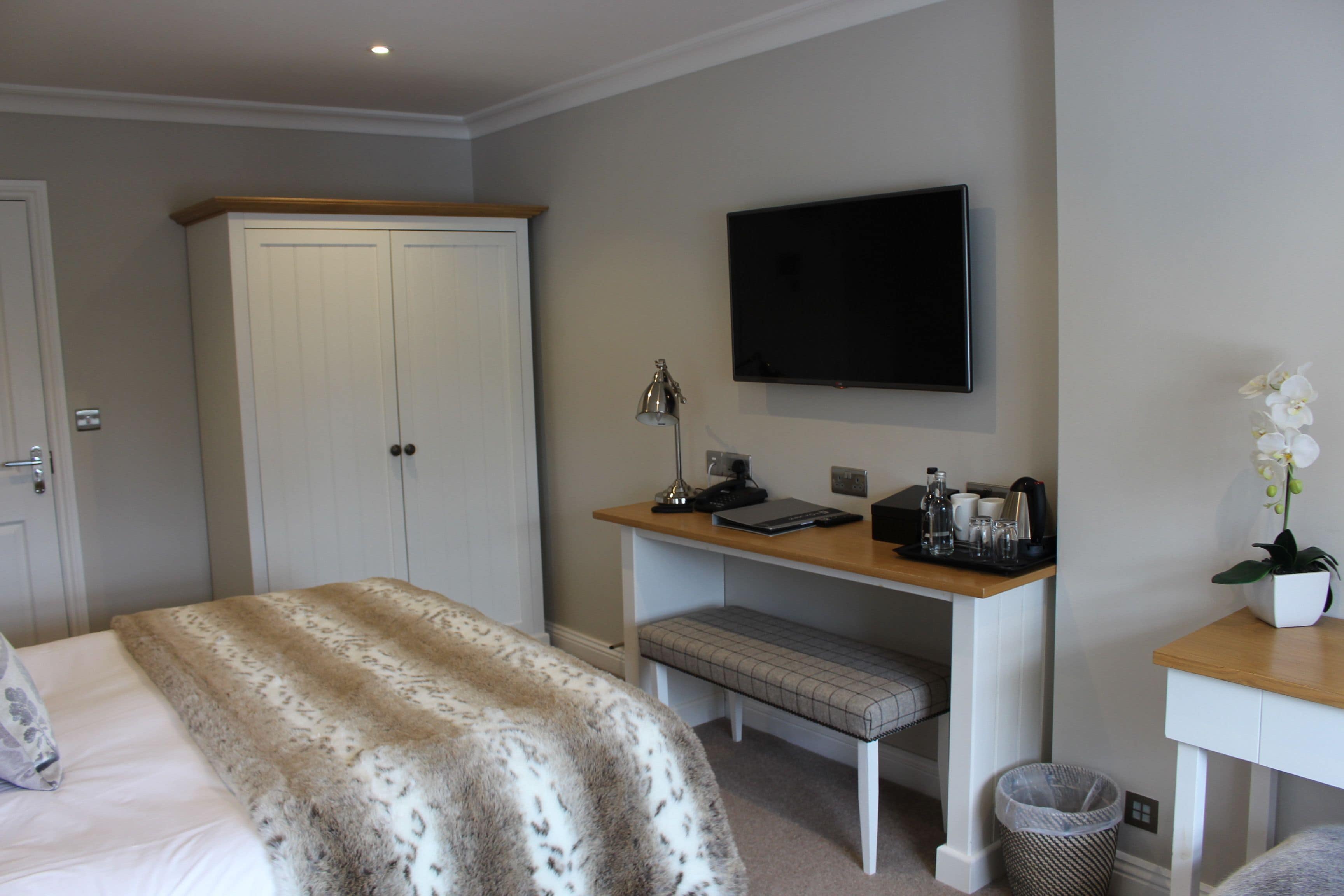 A bedroom with a bed, a desk with a computer, a TV, and a wardrobe.
