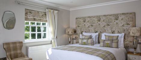 A bedroom with a large bed, a chair, a nightstand, and a window with curtains.