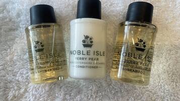 Three bottles of Noble Isle Perry Pear products on a white textured surface.
