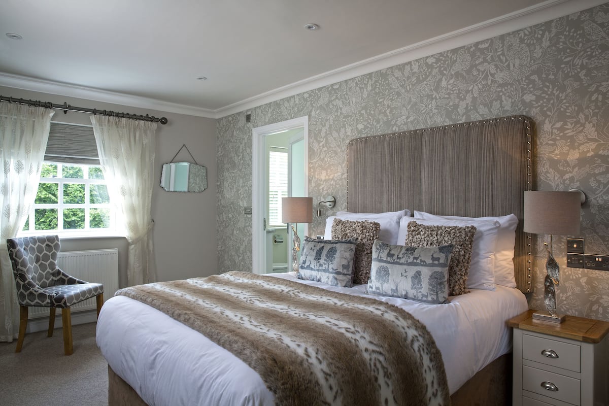 Une chambre à coucher avec un grand lit, une chaise, une table de chevet et une fenêtre avec des rideaux.