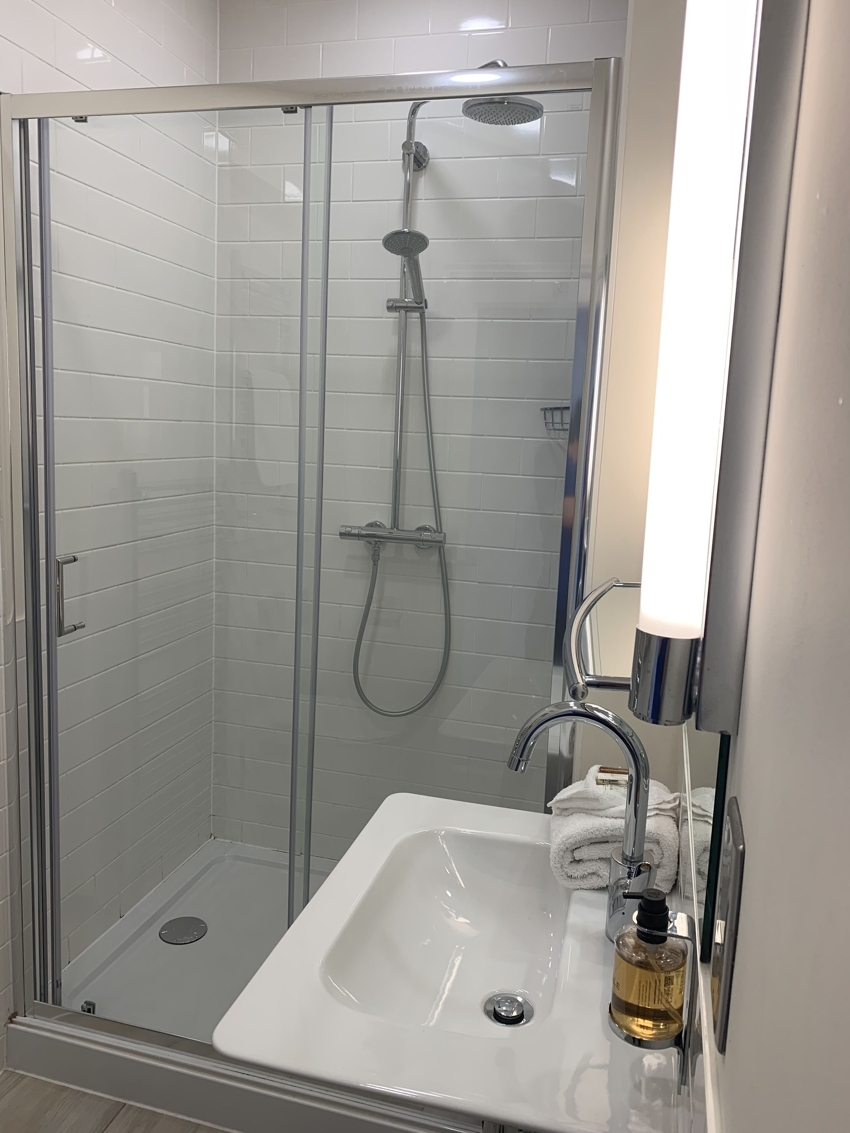 A modern bathroom with a glass-enclosed shower, a white sink, and a mirror with a light fixture.