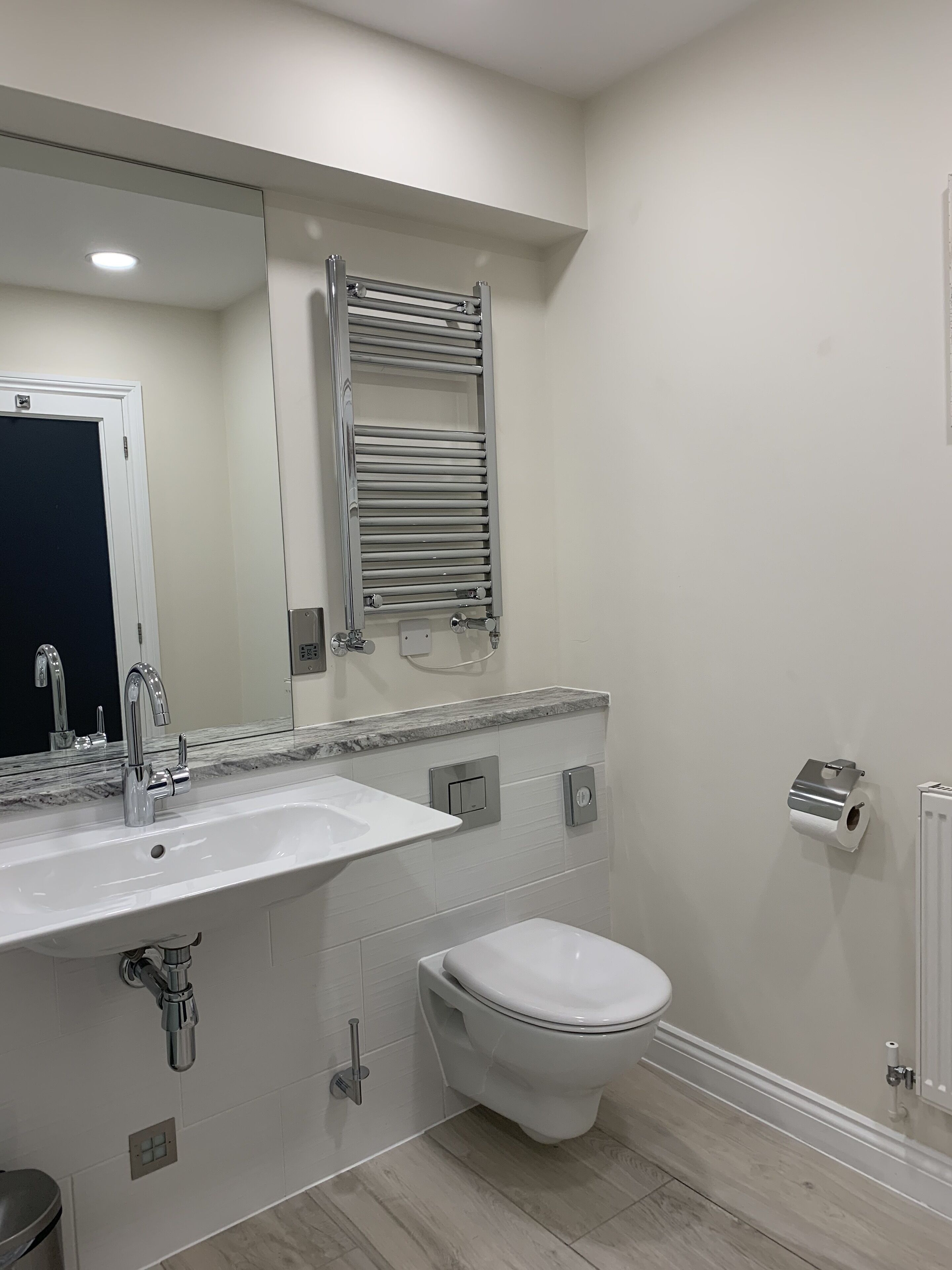 Une salle de bain moderne avec un lavabo blanc, des toilettes, un porte-serviettes et un miroir.
