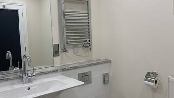 Une salle de bain moderne avec un lavabo blanc, des toilettes, un porte-serviettes et un miroir.