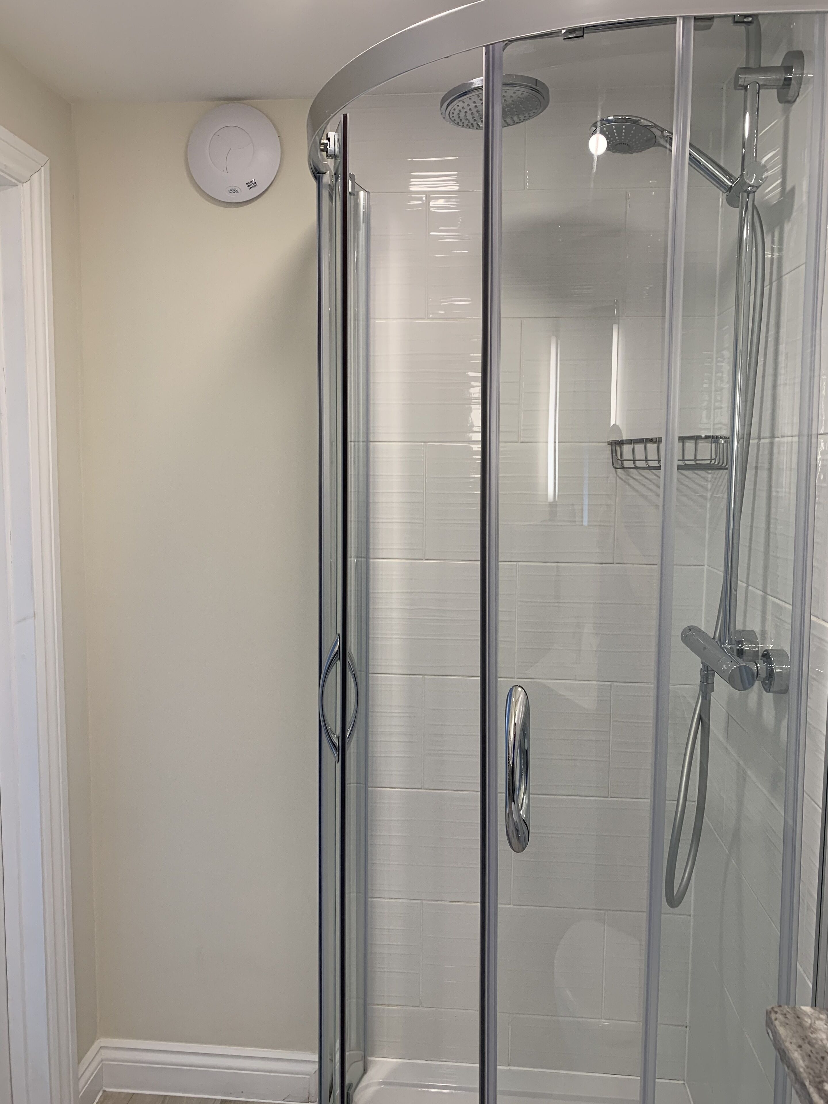 A glass-enclosed shower with a handheld showerhead and a wall-mounted faucet.