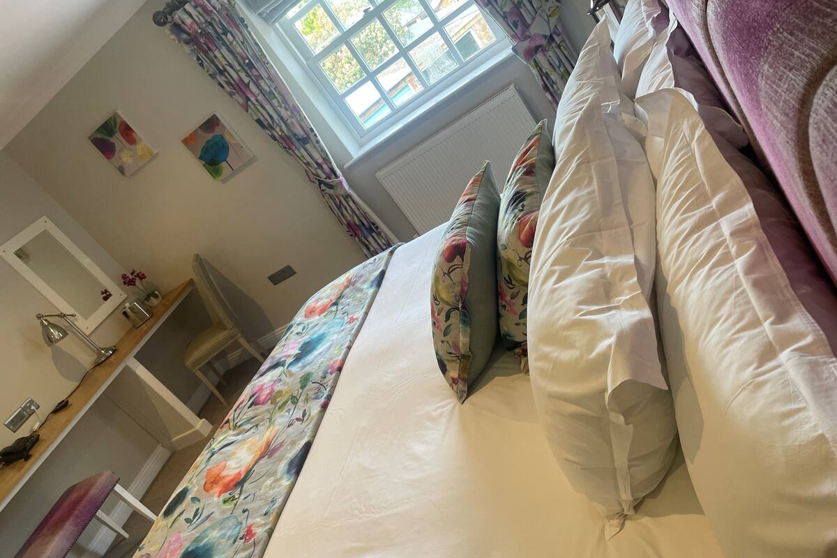 Une chambre à coucher avec un lit, des oreillers, une fenêtre et un miroir.
