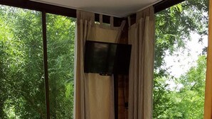 Une chambre avec un grand lit, un téléviseur fixé au mur et un balcon donnant sur la verdure.