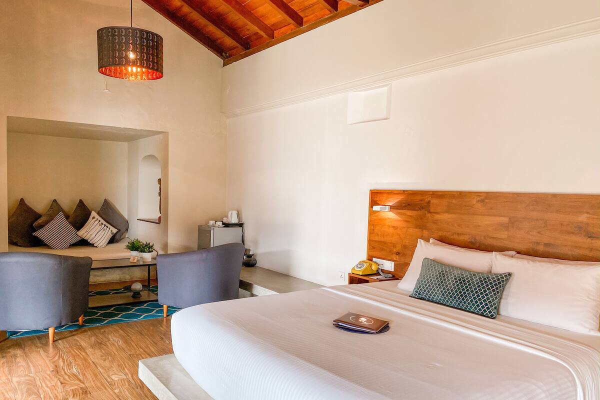 Una camera da letto con un letto grande, una testata in legno, un comodino con una lampada e un angolo salotto con un divano e poltrone.