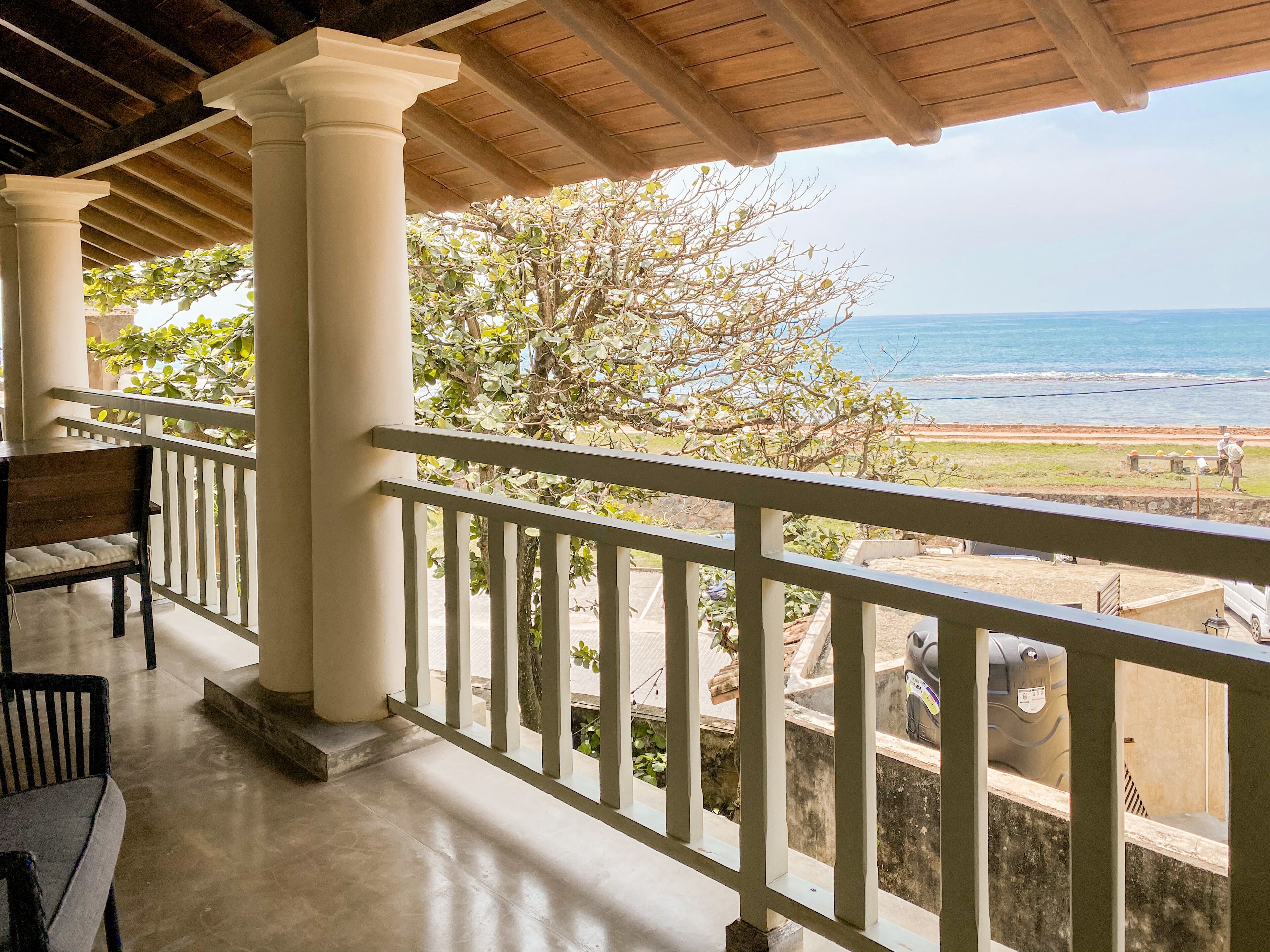A balcony with a view of the ocean, wooden columns, and a table with chairs.