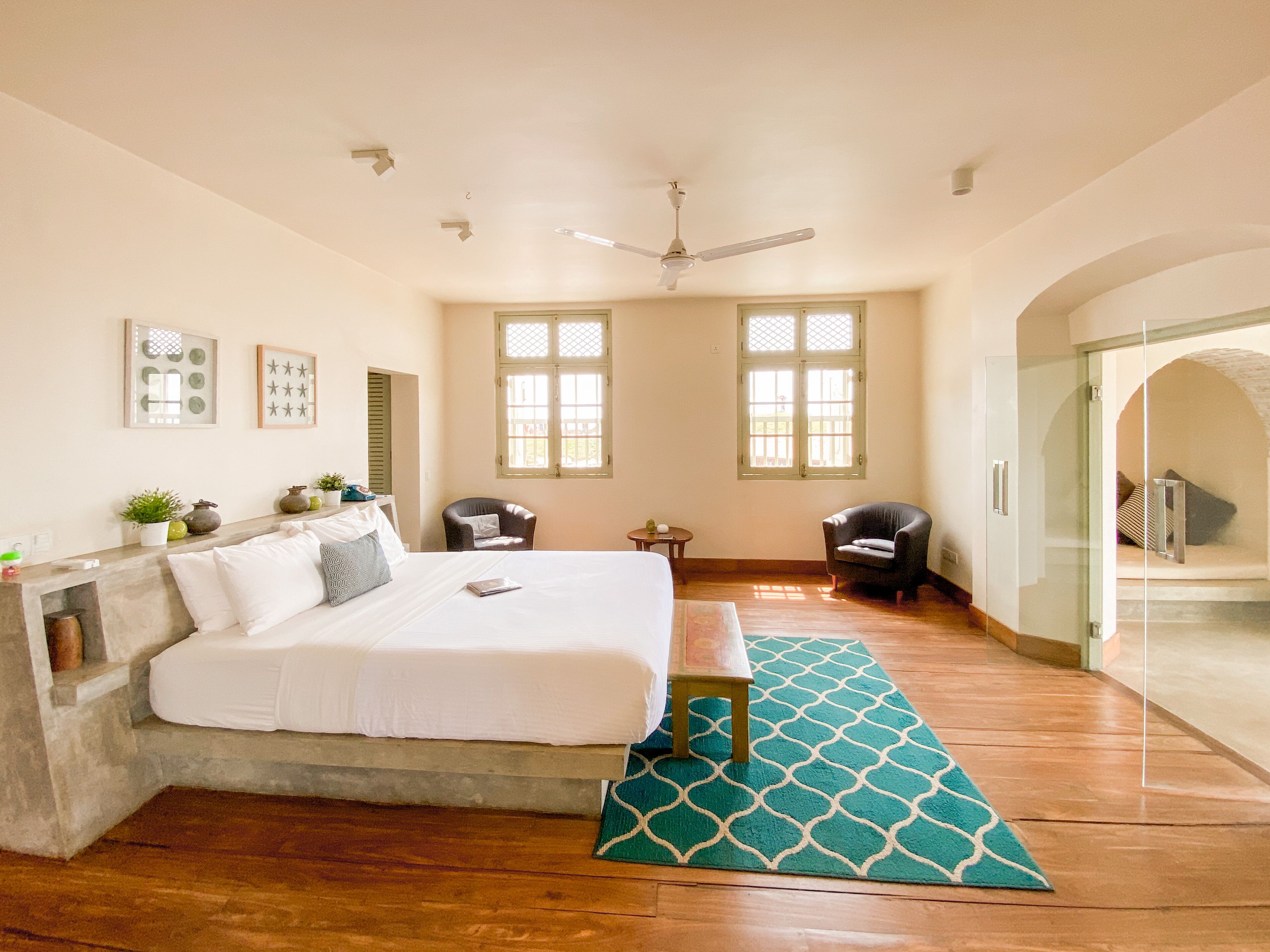 A bedroom with a bed, a desk, two chairs, a small table, and a window.
