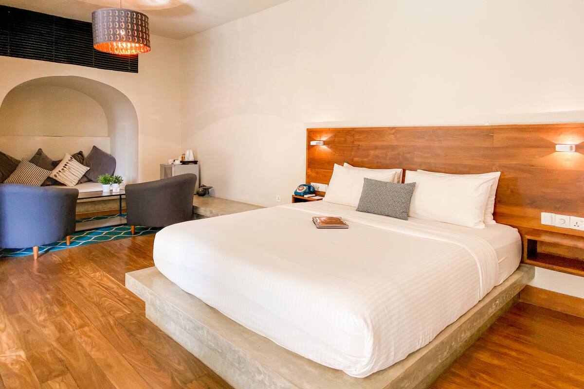Una camera d'albergo moderna con un letto grande, una testiera in legno, un'area salotto con un divano e poltrone, e un tavolino con una lampada.